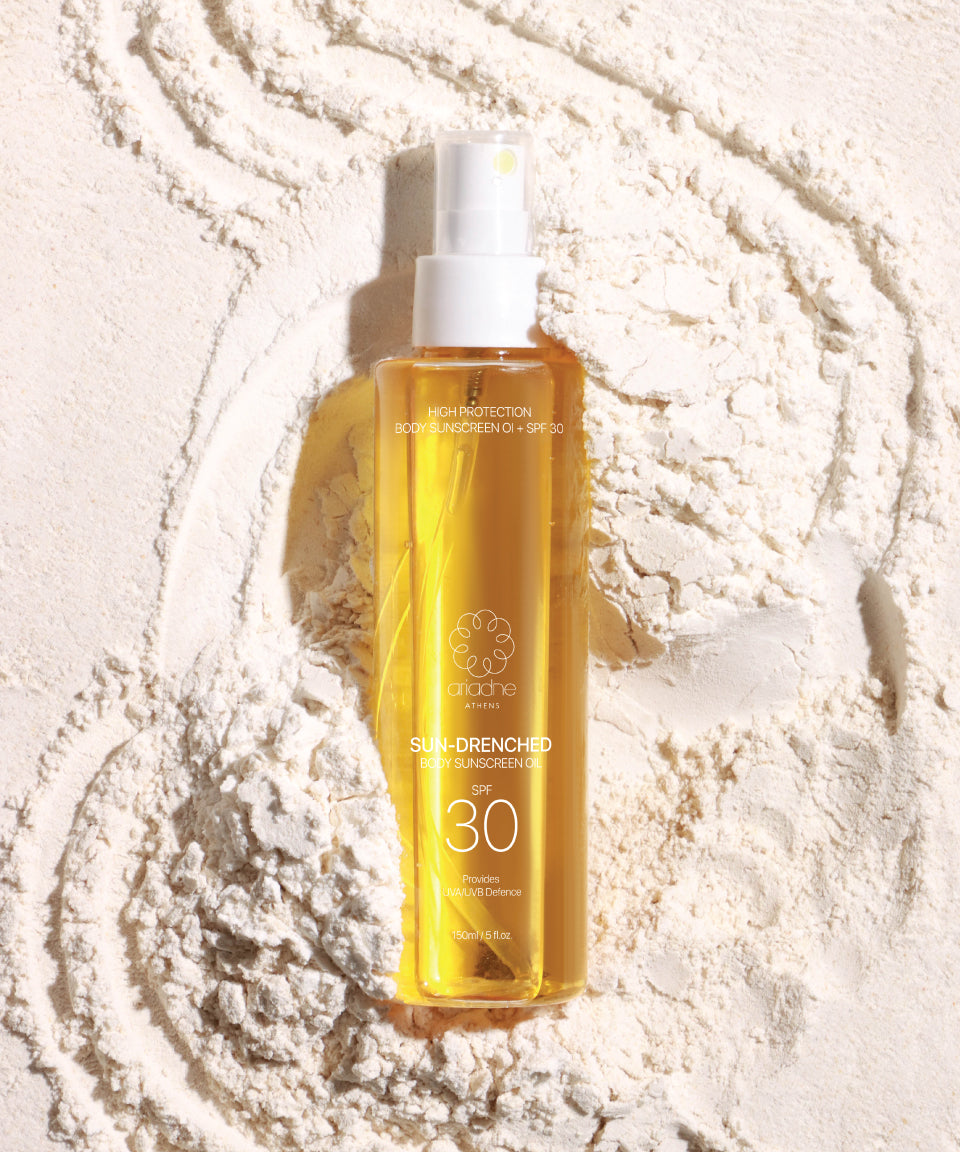 A bottle of Sun Drenched Body sunscreen oil on the sand.